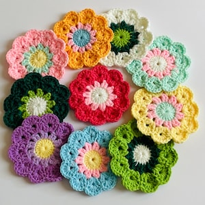 May include: A collection of ten circular, multi-colored crochet flower coasters. Each piece features a central core surrounded by contrasting petals in various shades including yellow, pink, green, red, purple, blue, and white, arranged in a cluster.