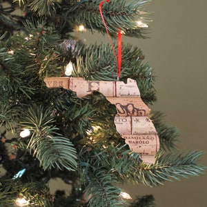 May include: A Christmas tree ornament shaped like the state of Florida, made from wine corks. The ornament is decorated with the words "VER", "predatory", "MILANO", and "BAROLO".