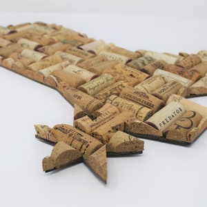 May include: A cork art piece shaped like the state of Texas with a star in the bottom left corner. The cork pieces are arranged in a mosaic pattern and have various wine labels and text on them. The text on the cork pieces includes "PREDATOR", "J.J.B.R.  MONDOVAN-PARKE", and "WORLD WINE".
