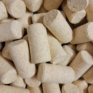 May include: A close-up image of a pile of natural cork bottle stoppers. The stoppers are all a light brown color and have a slightly rough texture.