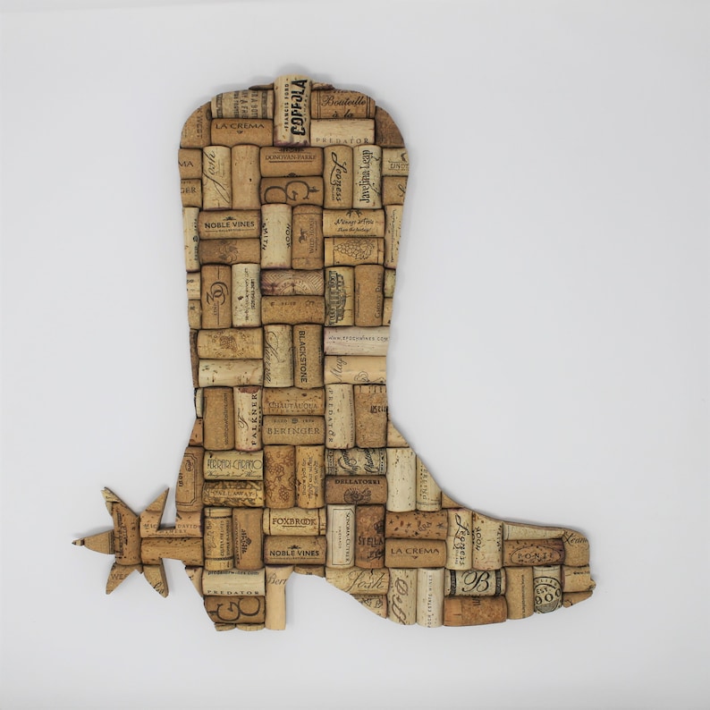 May include: A cowboy boot shaped wall art made from wine corks. The boot has a spur on the heel and is decorated with various wine cork labels.
