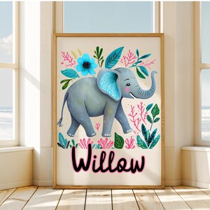 Puede incluir: Un cuadro enmarcado con un elefante gris con detalles azules, rodeado de ilustraciones florales y de hojas coloridas. El nombre "Willow" est&aacute; escrito en rosa. La obra de arte se exhibe en una habitaci&oacute;n con luz natural.