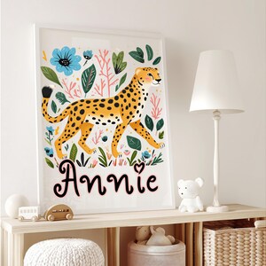 Puede incluir: Una impresi&oacute;n art&iacute;stica enmarcada que presenta un guepardo estilizado con pelaje amarillo y manchas negras, rodeado de flores y follaje coloridos. El nombre "Annie" est&aacute; escrito en cursiva debajo. La obra de arte se exhibe en una estanter&iacute;a.