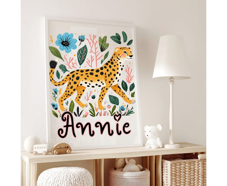 Puede incluir: Una impresi&oacute;n art&iacute;stica enmarcada que presenta un guepardo estilizado con pelaje amarillo y manchas negras, rodeado de flores y follaje coloridos. El nombre "Annie" est&aacute; escrito en cursiva debajo. La obra de arte se exhibe en una estanter&iacute;a.