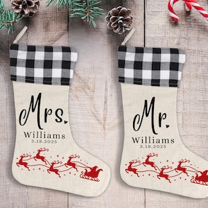 May include: Two Christmas stockings with a black and white checkered cuff and a beige body. One stocking says "Mrs. Williams" and the other says "Mr. Williams". Both have a red reindeer and sleigh design.