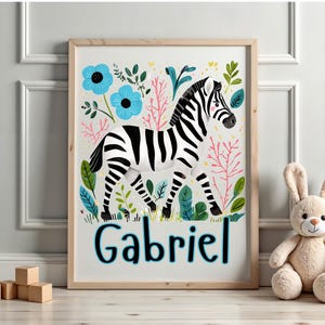 Puede incluir: Un cuadro enmarcado con una ilustraci&oacute;n de cebra a rayas blancas y negras, rodeada de flores azules y vegetaci&oacute;n. El nombre "Gabriel" est&aacute; escrito en azul en la parte inferior. Un peluche de conejo est&aacute; cerca.