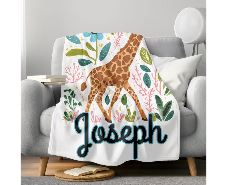 Peut inclure: Une couverture en polaire blanche avec une illustration color&eacute;e de girafe et des motifs floraux verts, roses et bleus. Le nom "Joseph" est &eacute;crit avec un contour bleu.