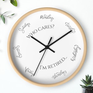 May include: A round wall clock with a light wood frame and a white face. The clock hands are black. The face has the words "Who Cares? I'm Retired..." and the days of the week in a cursive font.