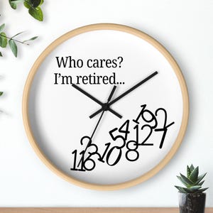 May include: A round wall clock with a light wood frame and a white face. The clock features black hands and black numbers in a unique, tilted arrangement. The text "Who cares? I'm retired..." is printed on the clock face.