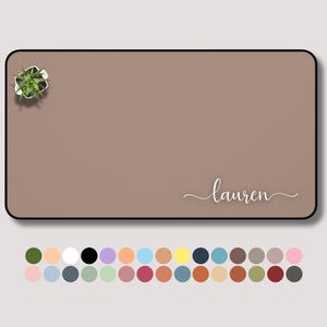 May include: A rectangular desk mat in a muted brown color with a black border. The name "Lauren" is written in a cursive font. A small potted plant is in the upper left corner. A color palette of various colors is at the bottom.