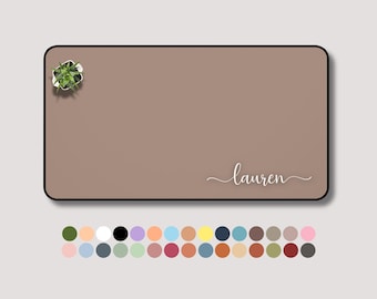 May include: A rectangular desk mat in a muted brown color with a black border. The name "Lauren" is written in a cursive font. A small potted plant is in the upper left corner. A color palette of various colors is at the bottom.