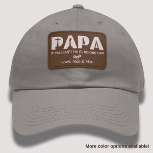 May include: Gray baseball cap with a brown patch that reads "PAPA" in white letters, along with the text "IF YOU CAN'T FIX IT, NO ONE CAN" and "Love, Alex & Mia." The cap has a curved brim and a button on top.