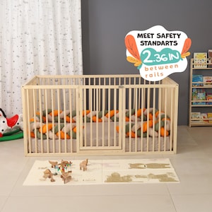 May include: A light-colored wooden baby playpen with vertical bars and a hinged door. The playpen contains a bed with a braided bumper in orange, green, and white. The text on the image reads "MEET SAFETY STANDARTS 2.36 IN between rails."