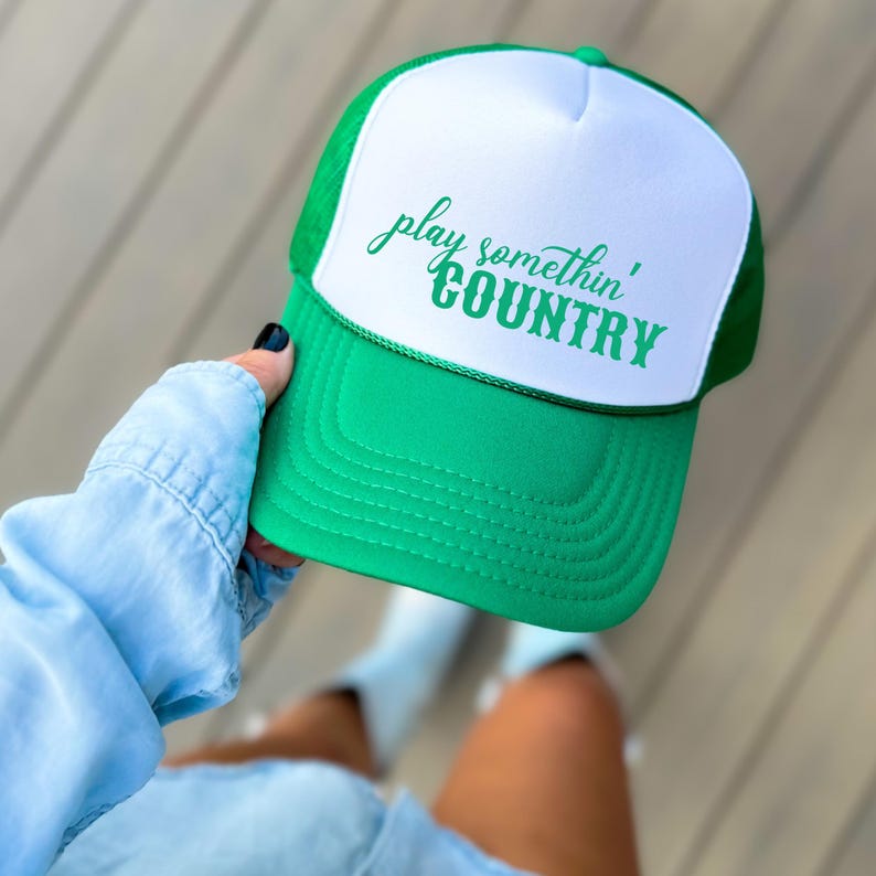 Puede incluir: Gorra de camionero verde y blanca con el texto "play somethin' COUNTRY" en verde. La gorra tiene una visera verde y una parte trasera de malla, con un panel frontal blanco. Estilo cl&aacute;sico.