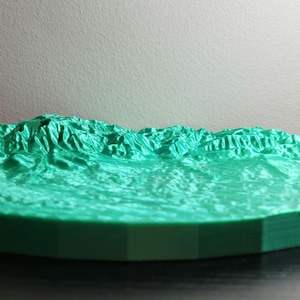 May include: A 3D printed model of a mountain range, with a green color scheme. The model is circular and has a layered base.