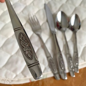 May include: A set of four silver-toned flatware pieces with a floral design. The pieces include a knife, fork, and two spoons.