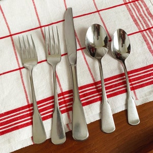 May include: Four pieces of silverware, including a knife, two forks, and a spoon, are laid out on a white and red checkered tablecloth. The silverware is made of polished metal and has a classic design.