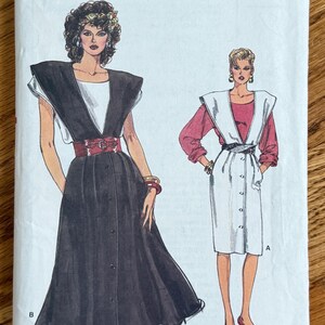 May include: A Very Easy Very Vogue sewing pattern envelope 9615 for sizes 8-10-12. The illustration shows two dress designs with wide shoulder details, button-front closures, and belts. One dress is black with a white top, the other is white with a red top.