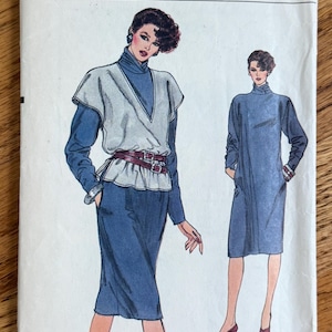 May include: A Very Easy Vogue sewing pattern envelope 8794 for sizes 8-10-12. The illustration shows two outfits: a blue long-sleeved dress with a high neck, and a blue long-sleeved dress paired with a light gray sleeveless wrap top and a dark red belt.