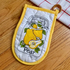 May include: Yellow quilted oven mitt with a white cotton panel featuring a drawing of a glass jar filled with pears and the word "Pear". The copyright text "HBI-1977" is printed below the word "Pear".