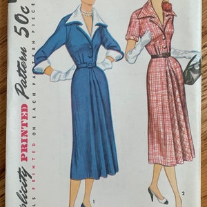 May include: Vintage Simplicity pattern envelope featuring illustrations of two dresses. One dress is a long-sleeved, blue dress with a white collar and cuffs. The other is a short-sleeved, red plaid dress. The envelope has the number 8377 and the text "Simplicity Printed Pattern 50c".