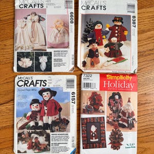 May include: Four McCall's Crafts and Simplicity Holiday sewing pattern envelopes featuring illustrations of fabric dolls, snowmen, angels, and holiday decor. The envelopes display product numbers 6608, 8387, 6157, and 7322 with various printed text and imagery.