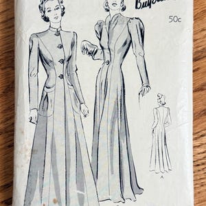 May include: A Butterick sewing pattern envelope, size 16, bust 34, featuring black and white illustrations of two long-sleeved, floor-length dresses. The front shows two variations, A and B, with button details and a back view. Text includes 1/85, 50c, and Follow the style trends with Butterick.