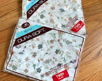 Puede incluir: Dos paquetes de sábanas Cannon Dura-Soft de tamaño doble. Las sábanas son blancas con un estampado floral y están etiquetadas como "No-Iron" y "Dura-Soft". Un paquete es para una sábana plana doble y el otro para una sábana bajera doble.