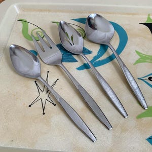 May include: Four silver utensils on a white tray with a blue and green design. The utensils include a fork, a slotted spoon, and two spoons.
