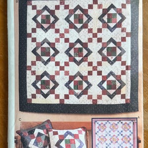 May include: A Butterick pattern envelope featuring a quilt and pillow design. The quilt has a repeating pattern of red, green, and black squares on a cream background. The pillows have a similar design. The envelope has the text "Butterick" and "5732".