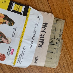 K&ouml;nnte beinhalten: Ein Vintage-N&auml;hmusterumschlag von McCall's f&uuml;r ein Damenkleid, Gr&ouml;&szlig;e 10, Brustumfang 82,5 cm. Die Musternummer lautet 2569 und der Preis betr&auml;gt 85 Cent. Der Umschlag ist gefaltet und zeigt die Vorderseite mit einer Zeichnung einer Frau in einem Kleid.