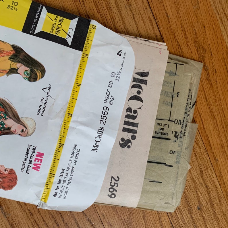 K&ouml;nnte beinhalten: Ein Vintage-N&auml;hmusterumschlag von McCall's f&uuml;r ein Damenkleid, Gr&ouml;&szlig;e 10, Brustumfang 82,5 cm. Die Musternummer lautet 2569 und der Preis betr&auml;gt 85 Cent. Der Umschlag ist gefaltet und zeigt die Vorderseite mit einer Zeichnung einer Frau in einem Kleid.
