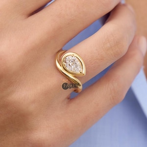 Anillo de compromiso de moissanita blanca curvada de 1,50 quilates con corte de pera y bisel único con garra. Oro amarillo de 18 quilates con forma de onda.