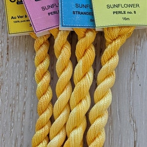 May include: Five spools of yellow embroidery floss, labeled "Chameleon Hand Colored Embroidery Threads" with the color name "Sunflower" and the thread type "Perle no. 8" and "Stranded".