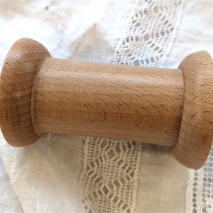 Puede incluir: Una bobina de madera con un acabado liso de color marrón claro. La bobina tiene una forma cilíndrica con extremos redondeados.
