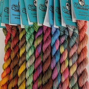 May include: Assortment of eight skeins of variegated embroidery floss in shades of brown, green, purple, blue, and pink. The floss is labelled "Chameleon Wild Berry Stranded Cotton 8m".
