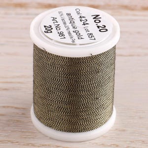 May include: A spool of antique gold thread, labeled "No. 20", "Col. 424 Lot. 857", "antique gold", "80% Viscose 20% metallis. Pes", "Art. No. 981", and "20g".