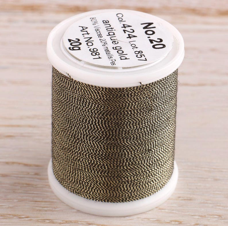 May include: A spool of antique gold thread, labeled "No. 20", "Col. 424 Lot. 857", "antique gold", "80% Viscose 20% metallis. Pes", "Art. No. 981", and "20g".