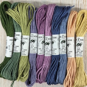 Puede incluir: Seis carretes de hilo de bordar en tonos de verde, morado, azul y naranja. Los carretes están etiquetados con "Soie d'Alger" e indican que el hilo es 100% seda. Los carretes están hechos en París, Francia.