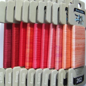 Puede incluir: Una colecci&oacute;n de 14 carretes de cinta de seda de 4 mm de ancho en tonos de rojo, naranja y rosa. Los carretes est&aacute;n etiquetados con "4 mm" y el embalaje incluye el texto "River Silks 4 mm-Satin/Satin 5 yards Premium Hand Dyed 100% Silk Ribbon Made in China 262".