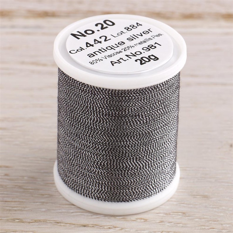May include: A spool of No. 20 antique silver thread, labeled "Col. 442 Lot. 884 antique silver 80% Viscose 20% metallic Pes. Art. No. 981 20g".
