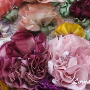 May include: A close-up of a handmade silk ribbon embroidery featuring a variety of flowers in shades of pink, purple, and green. The flowers are arranged in a cluster and have a delicate, three-dimensional appearance. The embroidery is signed "Lorna Bateman Embroidery".