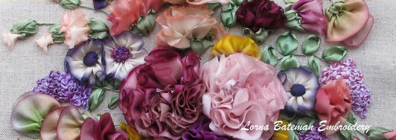 May include: A close-up of a handmade silk ribbon embroidery featuring a variety of flowers in shades of pink, purple, and green. The flowers are arranged in a cluster and have a delicate, three-dimensional appearance. The embroidery is signed "Lorna Bateman Embroidery".