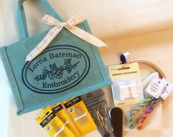 Könnte beinhalten: Eine türkisfarbene Tragetasche mit dem Text "Lorna Bateman Embroidery" in weißen Buchstaben. Die Tasche ist gefüllt mit Stickzubehör, darunter Nadeln, Garn und einen Stickrahmen.