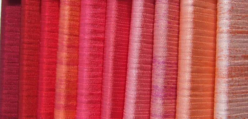 Puede incluir: Una colecci&oacute;n de muestras de tela en varios tonos de rojo, naranja y rosa. La tela tiene un sutil patr&oacute;n a rayas.