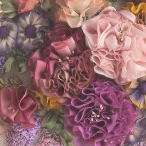 May include: Close-up of a floral arrangement made of fabric flowers. The flowers are in shades of pink, purple, and burgundy. The flowers are arranged in a cluster and have a delicate, ruffled texture.
