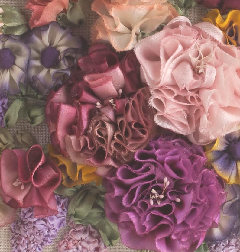 May include: Close-up of a floral arrangement made of fabric flowers. The flowers are in shades of pink, purple, and burgundy. The flowers are arranged in a cluster and have a delicate, ruffled texture.