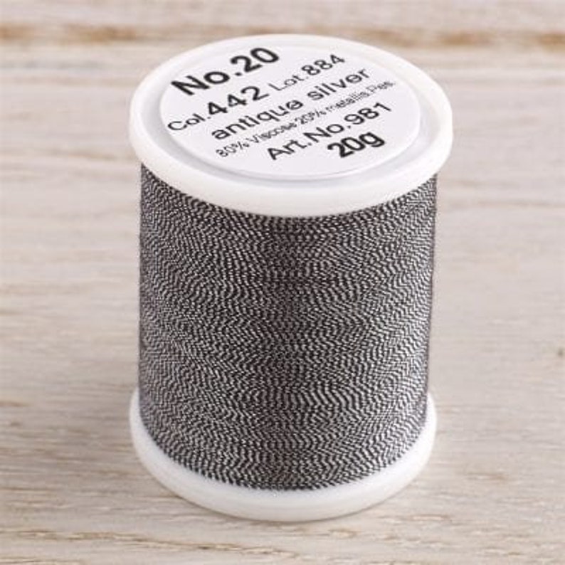 K&ouml;nnte beinhalten: Eine Spule mit No. 20 antikem Silbergarn, beschriftet mit Col. 442 Lot. 884, 80% Viskose 20% metallische Fasern, Art. No. 981, 20g.