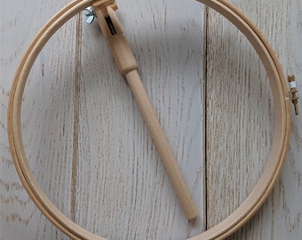 May include: A wooden embroidery hoop with a tightening knob and a wooden tightening tool. The hoop is on a white wooden surface.