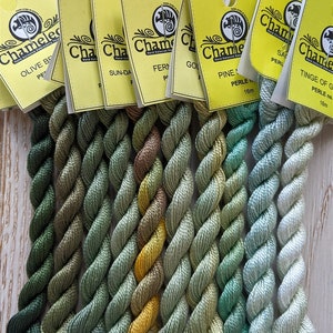 May include: Ten spools of Chameleon Hand-Dyed Embroidery Floss in shades of green, yellow, and blue. The floss is wound around cards with the Chameleon logo and the color number and name.